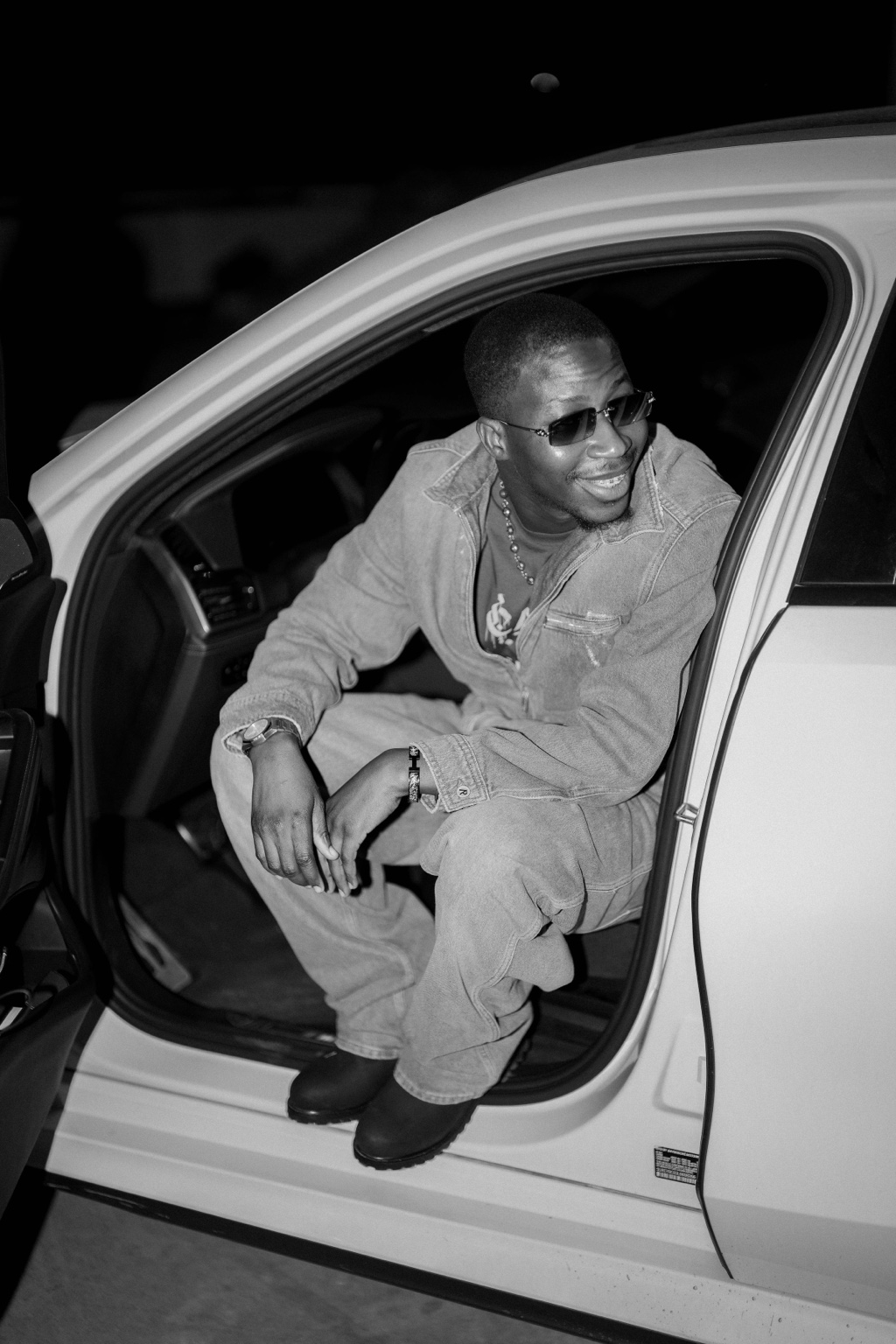 LL Degree seated in a vehicle doorway in a black-and-white press photograph